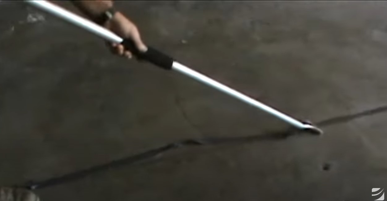 A person holds a long, white cane while tracing a line on a concrete surface.