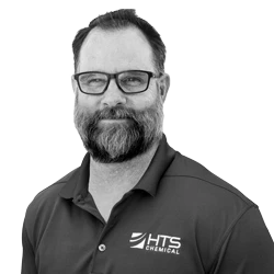 A smiling man with glasses and a beard is wearing a dark polo shirt featuring the logo of HTS Chemical. He poses against a light background.