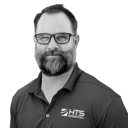 A smiling man with glasses and a beard is wearing a dark polo shirt featuring the logo of HTS Chemical. He poses against a light background.